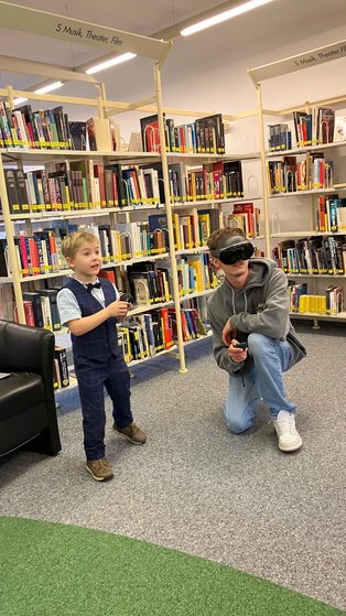 Ein kleiner Junge schaut fasziniert, ein junger Mann hockt neben ihm und spielt mit der VR-Brille